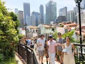 Groups whjo stroll along a leafy elevated path, with traditional red-roofed shophouses in the foreground and Singapore’s modern skyscrapers rising in the background.